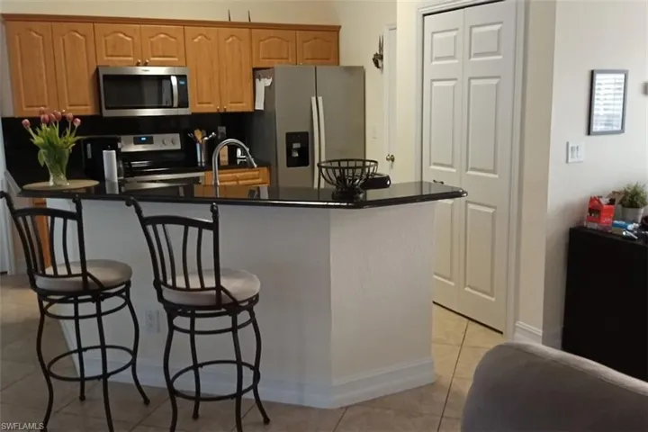 Kitchen featuring appliances with stainless steel finishes, a kitchen bar, light tile patterned floors, dark countertops, and a kitchen island with sink