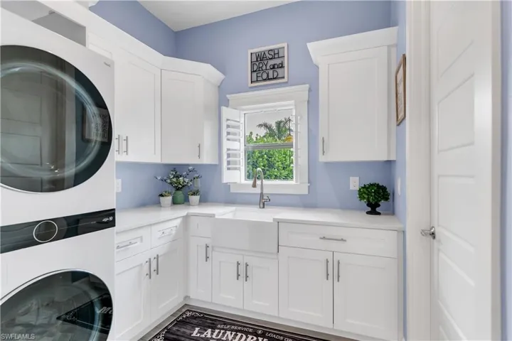 Laundry area with stacked washer / dryer, cabinets, sink, and hardwood / wood-style floors