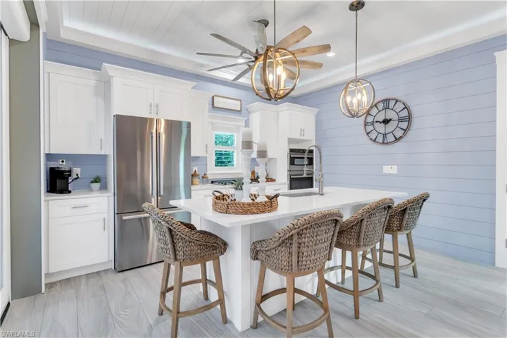 Kitchen featuring ceiling fan, light hardwood / wood-style floors, an island with sink, stainless steel appliances, and hanging light fixtures