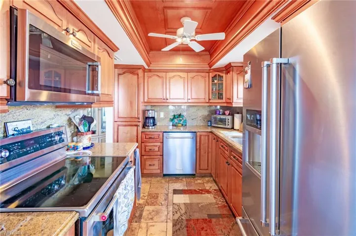 Kitchen with decorative backsplash, appliances with stainless steel finishes, light stone counters, a raised ceiling, and crown molding