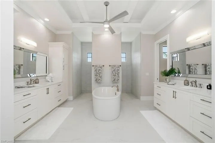Primary bathroom featuring a soaking tub, ceiling fan, walk in shower, two vanities, and crown molding