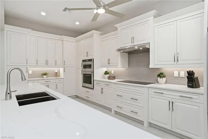 Kitchen with light quartz countertops, white cabinets, stainless steel double oven, and under cabinet lighting