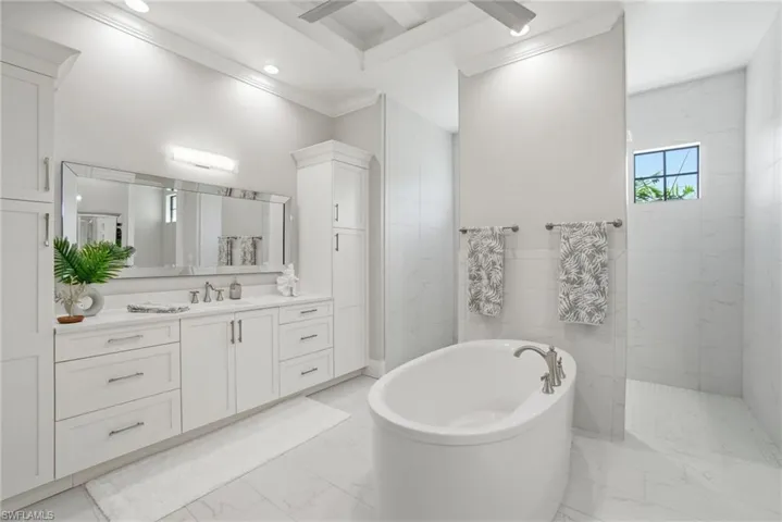 Primary bathroom featuring a soaking tub, vanity, ornamental molding, a marble finish shower, and light marble finish flooring