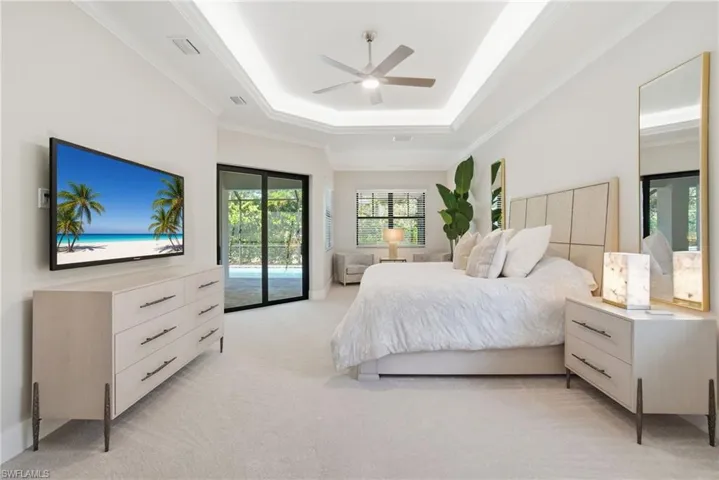 Primary Bedroom featuring access to exterior lanai and pool, ornamental molding, light carpet, a tray ceiling, and a ceiling fan