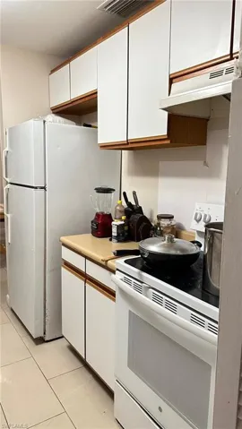 Kitchen with white range with electric cooktop, white cabinets, light countertops, light tile patterned floors, and under cabinet range hood