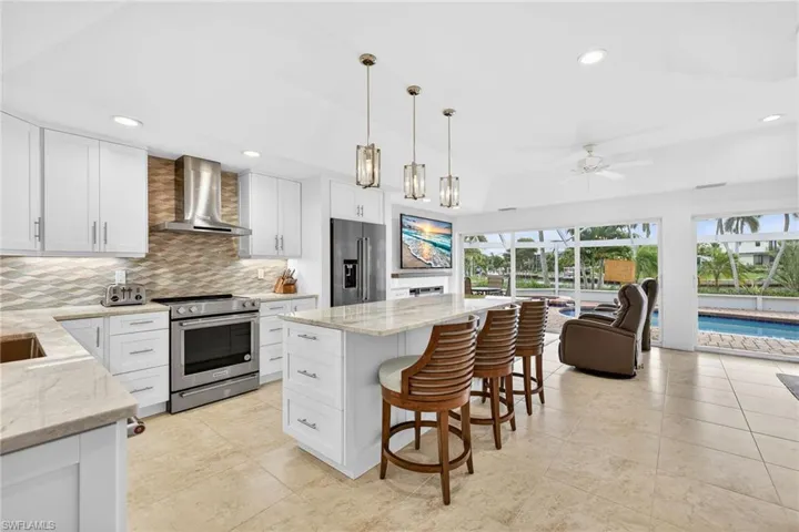 Kitchen with a kitchen bar, a center island, white cabinetry, appliances with stainless steel finishes, and light stone counters