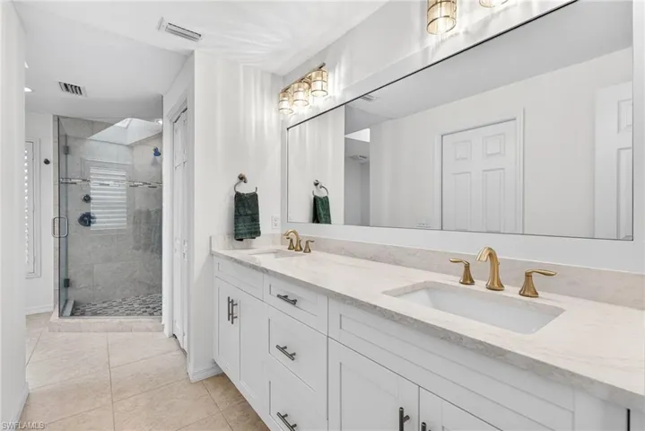 Primary Bathroom with double vanity, a shower stall, light tile patterned flooring, and a closet