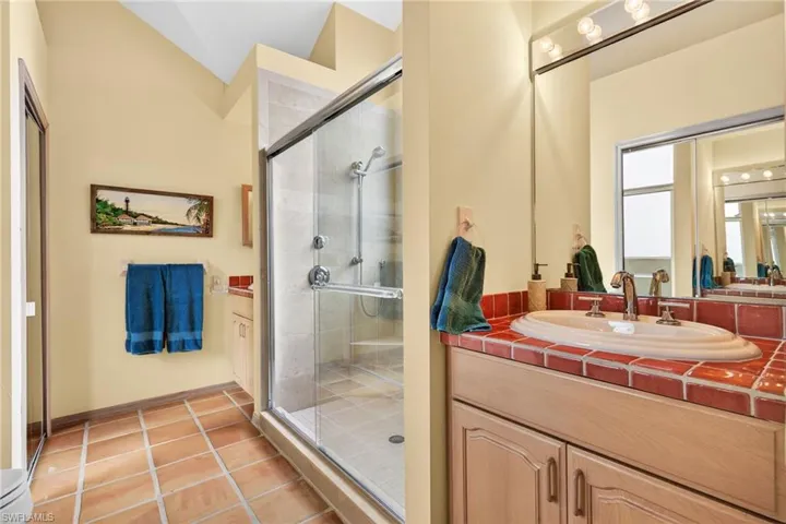 Bathroom with vanity, a stall shower, light tile patterned floors, and vaulted ceiling