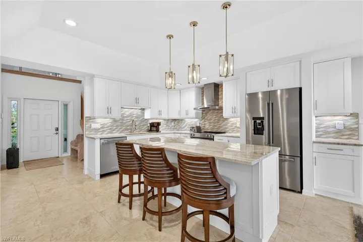 Kitchen featuring stainless steel appliances, white cabinets, a breakfast bar, light stone counters, and decorative light fixtures