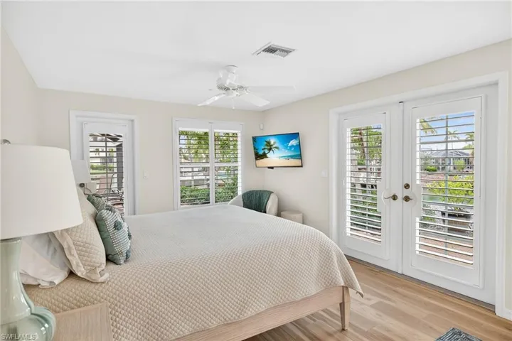 Bedroom featuring access to exterior, french doors, light wood-style floors, a ceiling fan, and multiple windows