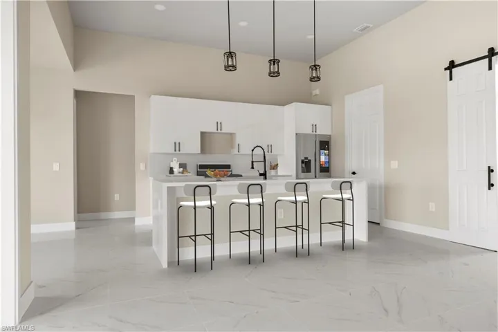 Kitchen featuring stainless steel fridge with ice dispenser, a towering ceiling, light marble finish flooring, an island with sink, and white cabinetry