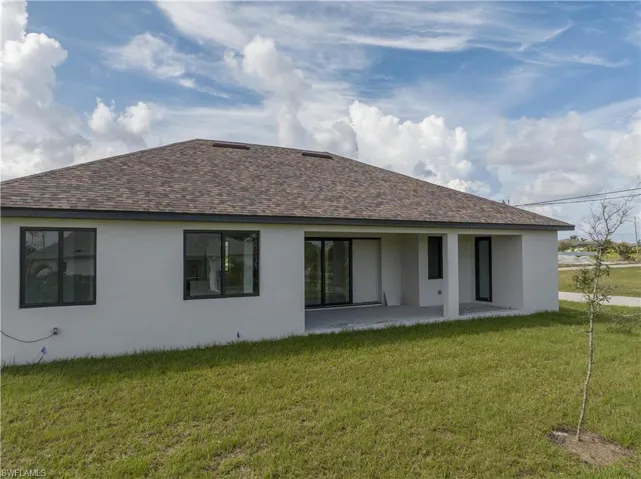 Back of house with a shingled roof, a patio area, stucco siding, and a lawn