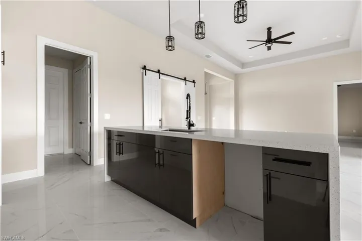 Kitchen featuring a barn door, ceiling fan, light marble finish flooring, hanging light fixtures, and modern cabinets