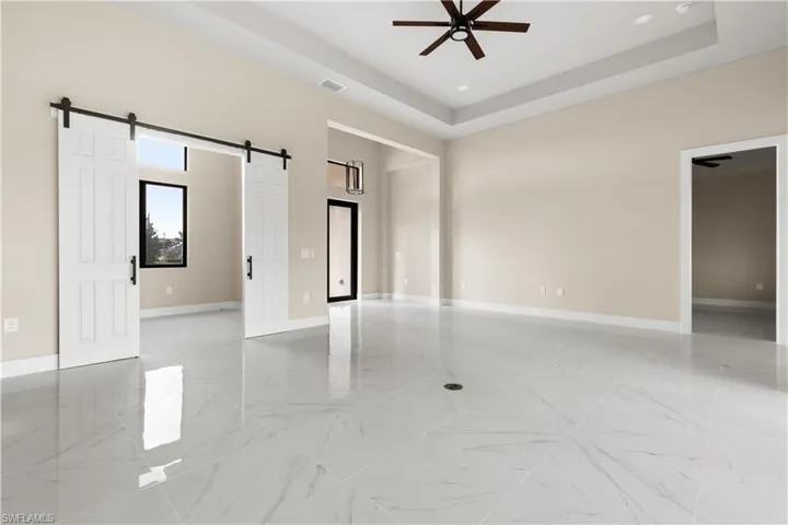 Empty room with a barn door, light marble finish flooring, a ceiling fan, a tray ceiling, and recessed lighting