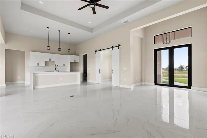 Unfurnished living room with a high ceiling, light marble finish floors, a barn door, recessed lighting, and a ceiling fan