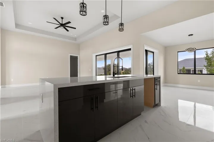 Kitchen featuring modern cabinets, dark cabinetry, light marble finish flooring, a kitchen island, and pendant lighting