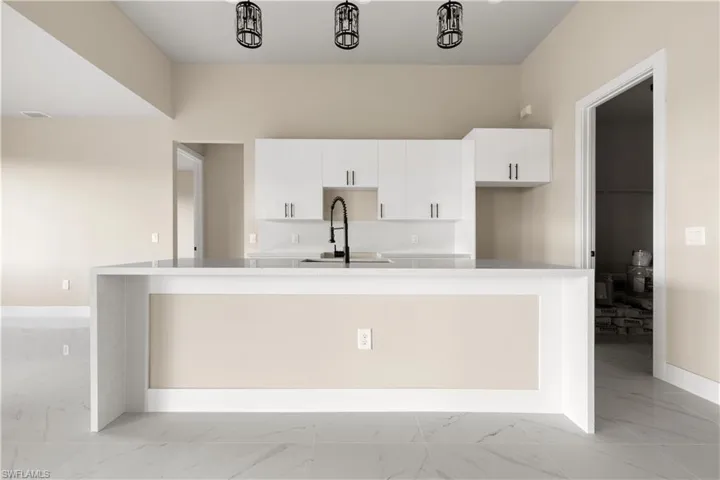 Kitchen with light marble finish floors, white cabinetry, a kitchen island with sink, and light countertops