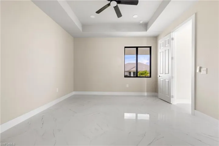 Unfurnished bedroom featuring light marble finish floors, a tray ceiling, recessed lighting, and ceiling fan