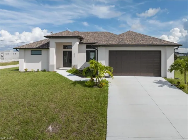 Prairie-style house with stucco siding, a front yard, an attached garage, driveway, and roof with shingles