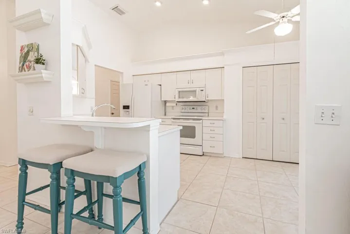 Kitchen featuring kitchen peninsula, a breakfast bar, white appliances, white cabinets, and lofted ceiling