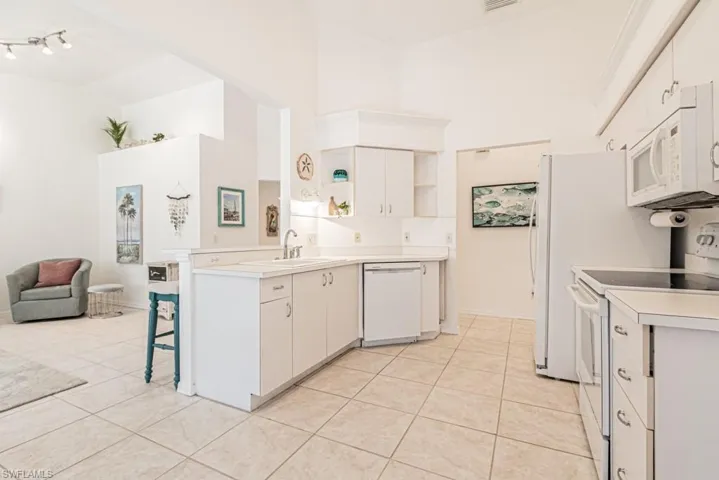 Kitchen with white cabinetry, white appliances, sink, and light tile patterned floors