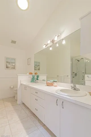 Master Bathroom with tile patterned flooring, lofted ceiling, toilet, vanity, and a shower with shower door
