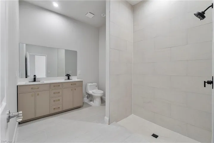 Full bath with tiled shower, double vanity, a sink, and toilet