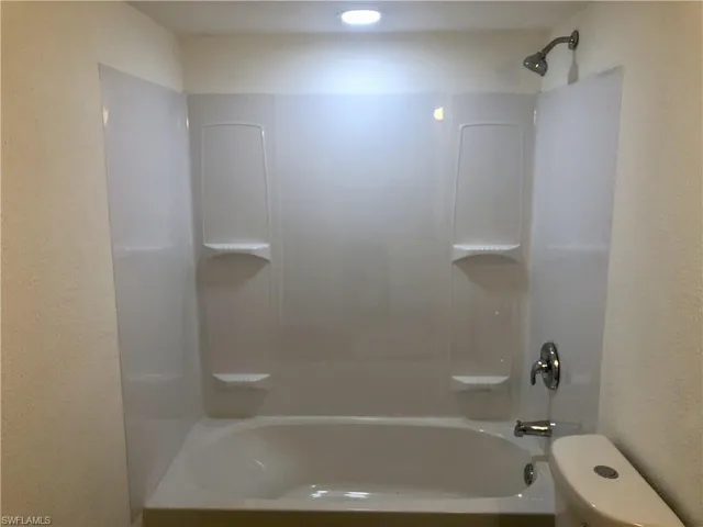White bathtub with a coordinating shower surround featuring integrated shelving
