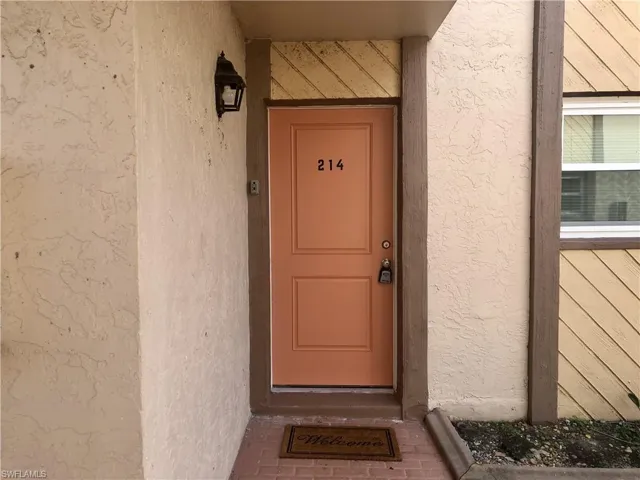 Entry door featuring a panel design, a numeric address, and a wall-mounted exterior light fixture
