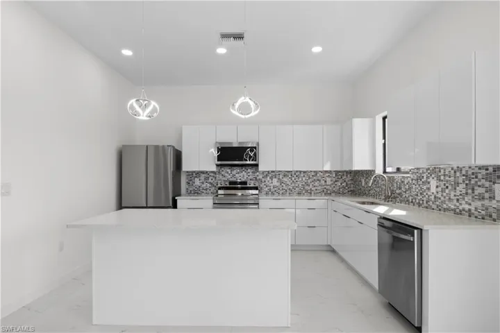 Kitchen with decorative light fixtures, light marble finish floors, appliances with stainless steel finishes, modern cabinets, and white cabinets