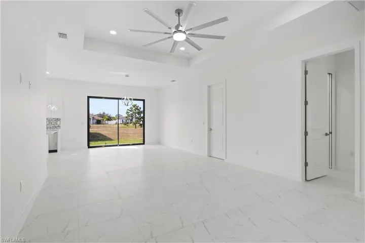 Empty room featuring recessed lighting, light marble finish flooring, a tray ceiling, and a ceiling fan