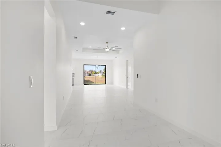 Corridor with light marble finish floors, recessed lighting, and a tray ceiling