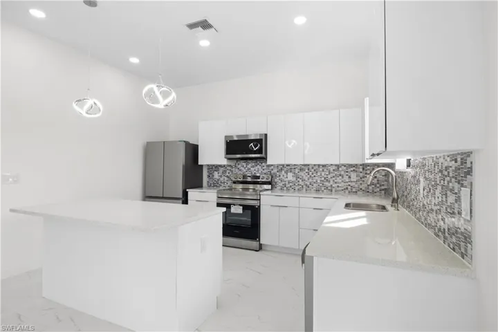 Kitchen featuring stainless steel appliances, pendant lighting, white cabinetry, a kitchen island, and light marble finish flooring