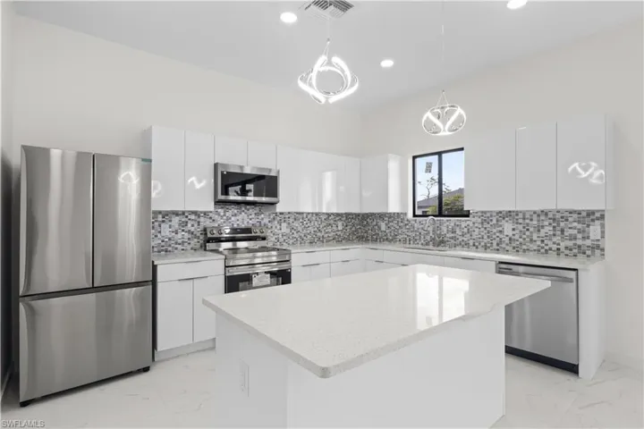 Kitchen featuring stainless steel appliances, light marble finish flooring, decorative light fixtures, white cabinetry, and modern cabinets