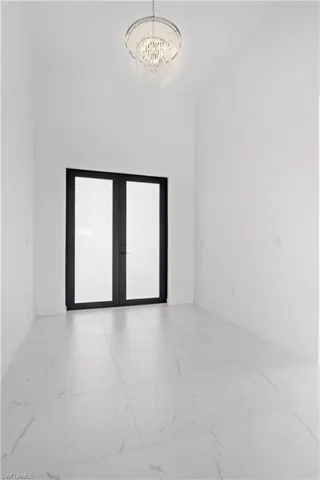 Spare room featuring light marble finish floors, french doors, and a chandelier