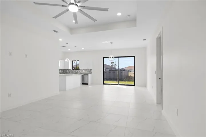 Unfurnished living room featuring a raised ceiling, light marble finish flooring, a ceiling fan, and recessed lighting
