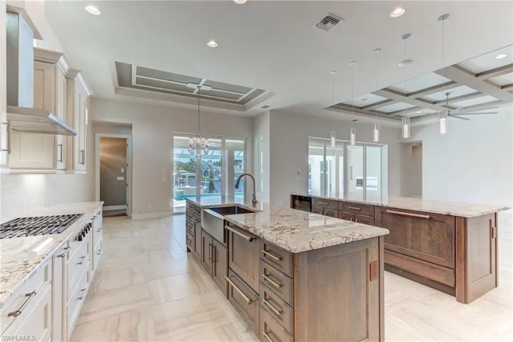 Kitchen featuring hanging light fixtures, light stone counters, recessed lighting, wall chimney exhaust hood, and a chandelier