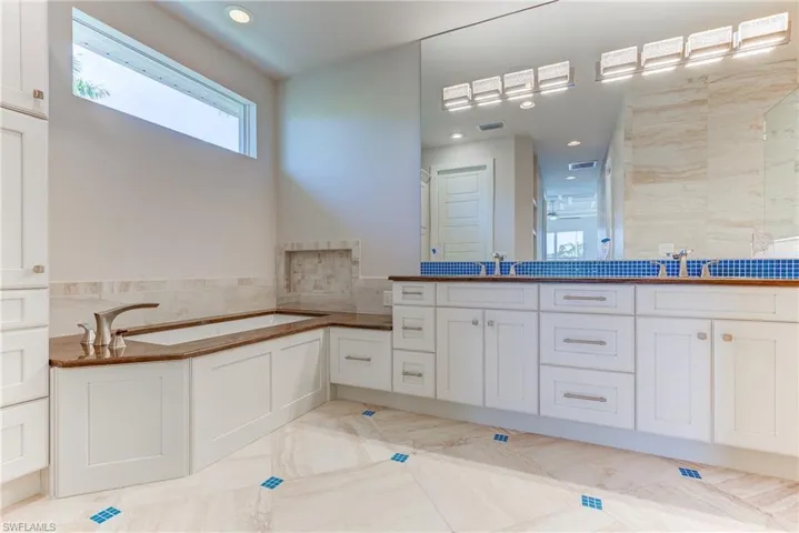 Full bath featuring double vanity, a garden tub, tile walls, and recessed lighting