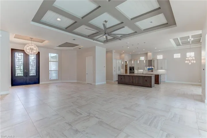 Unfurnished living room featuring a chandelier, healthy amount of natural light, ceiling fan, coffered ceiling, and a raised ceiling