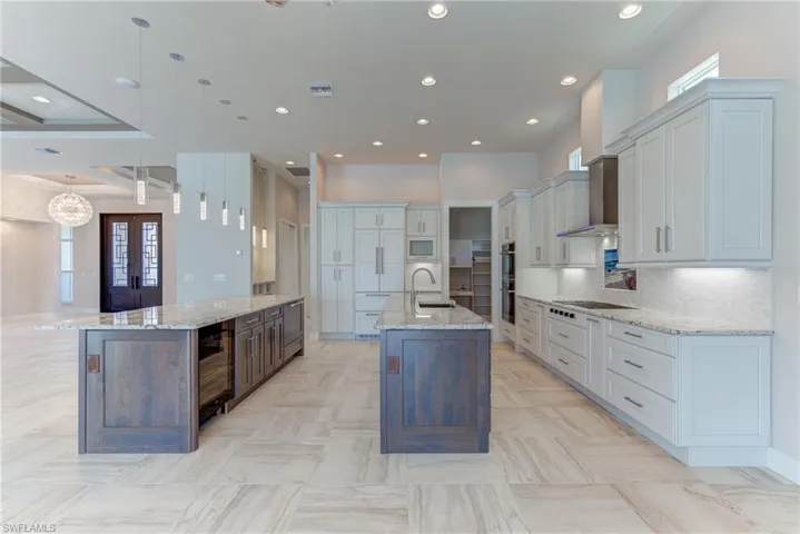 Kitchen with light stone countertops, pendant lighting, decorative backsplash, wine cooler, and recessed lighting