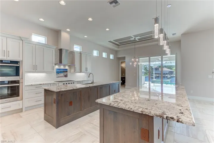 Kitchen featuring light stone countertops, double oven, decorative light fixtures, recessed lighting, and wall chimney exhaust hood