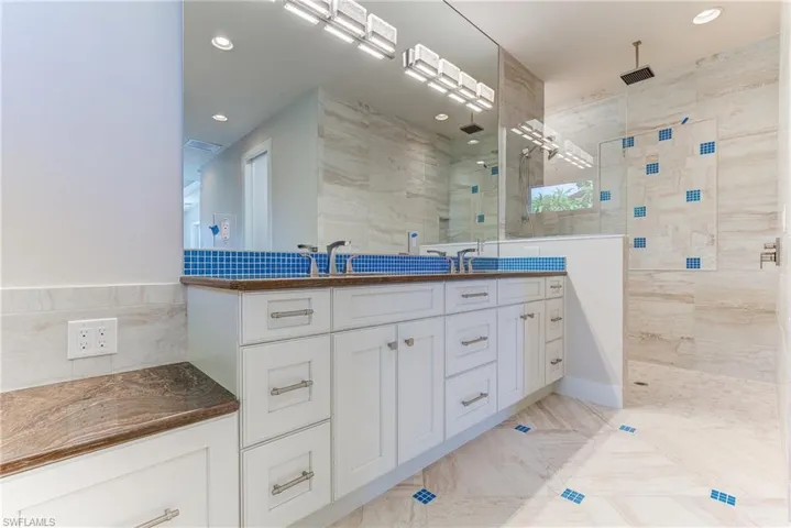 Bathroom featuring double vanity, walk in shower, tile walls, and recessed lighting