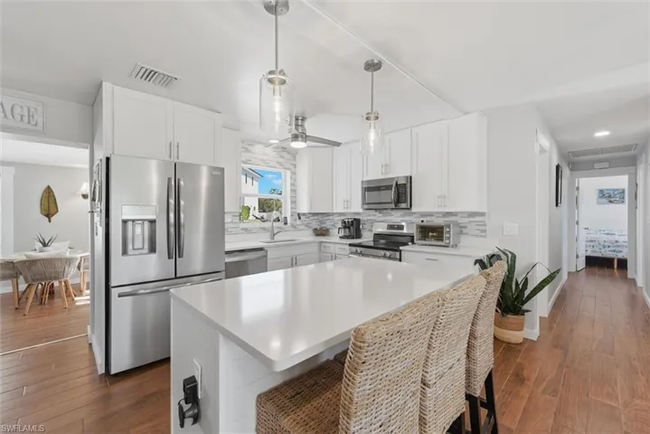 Kitchen with stainless steel appliances, decorative backsplash, dark wood-style flooring, a breakfast bar area, and white cabinets