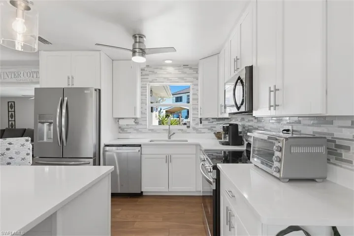 Kitchen with white cabinetry, stainless steel appliances, light wood-style floors, a ceiling fan, and tasteful backsplash