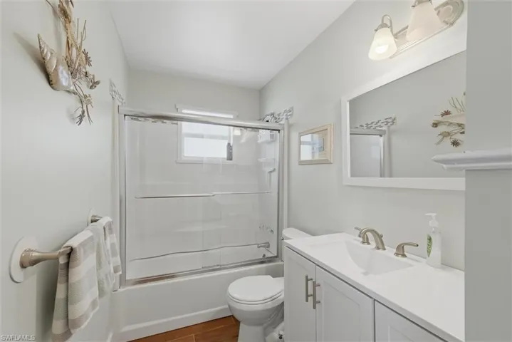 Full bathroom with enclosed tub / shower combo, vanity, and dark wood-type flooring