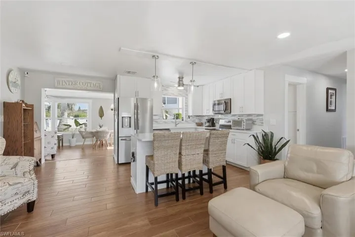 Kitchen featuring open floor plan, stainless steel appliances, a kitchen island, white cabinets, and dark wood-type flooring