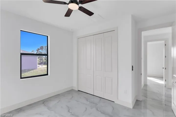 Unfurnished bedroom with a closet, baseboards, marble finish floor, and ceiling fan