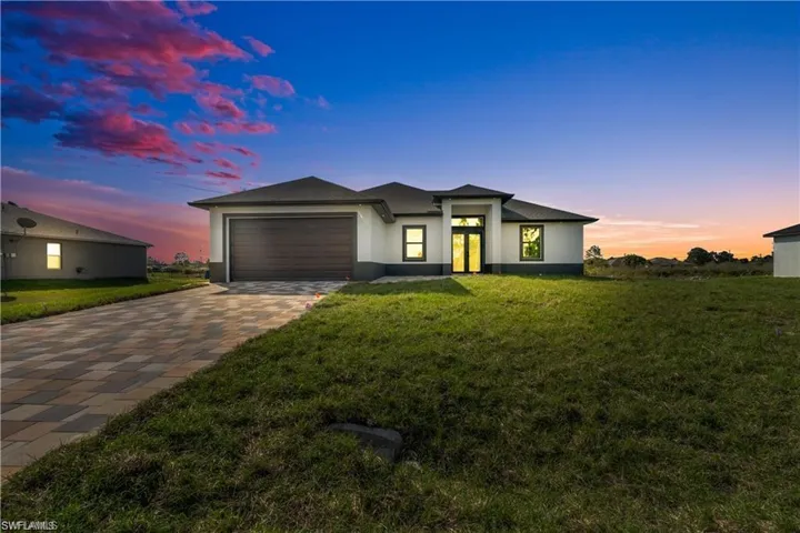 Prairie-style home featuring an attached garage, a lawn, stucco siding, and decorative driveway