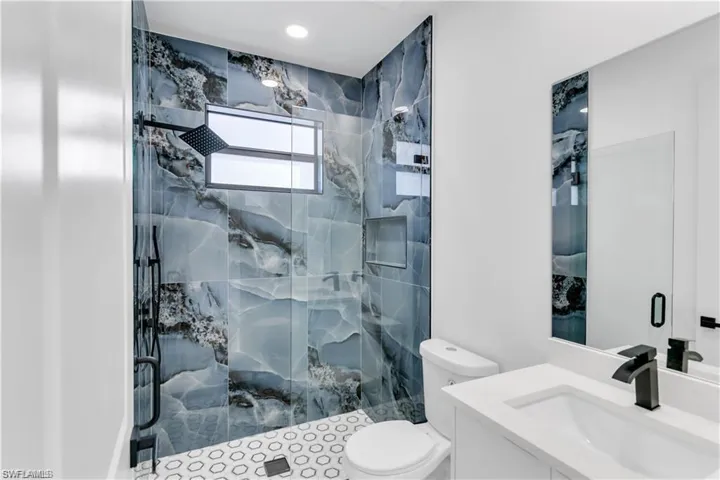 Bathroom featuring toilet, a marble finish shower, and vanity