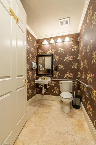 Half bath with a textured ceiling, wallpapered walls, and toilet